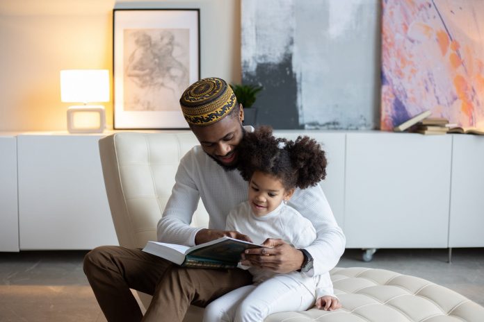 smiling black father reading book to adorable daughter